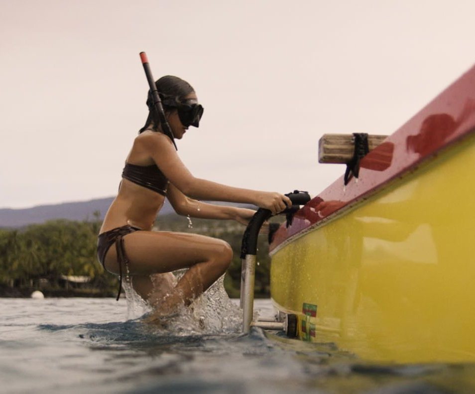 Woman in a bikini climbs out of a yellow boat wearing a snorkel mask in the ocean.