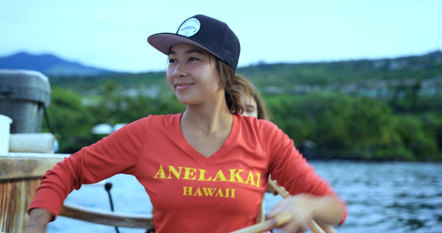 Woman in red shirt and cap on boat, smiling. 