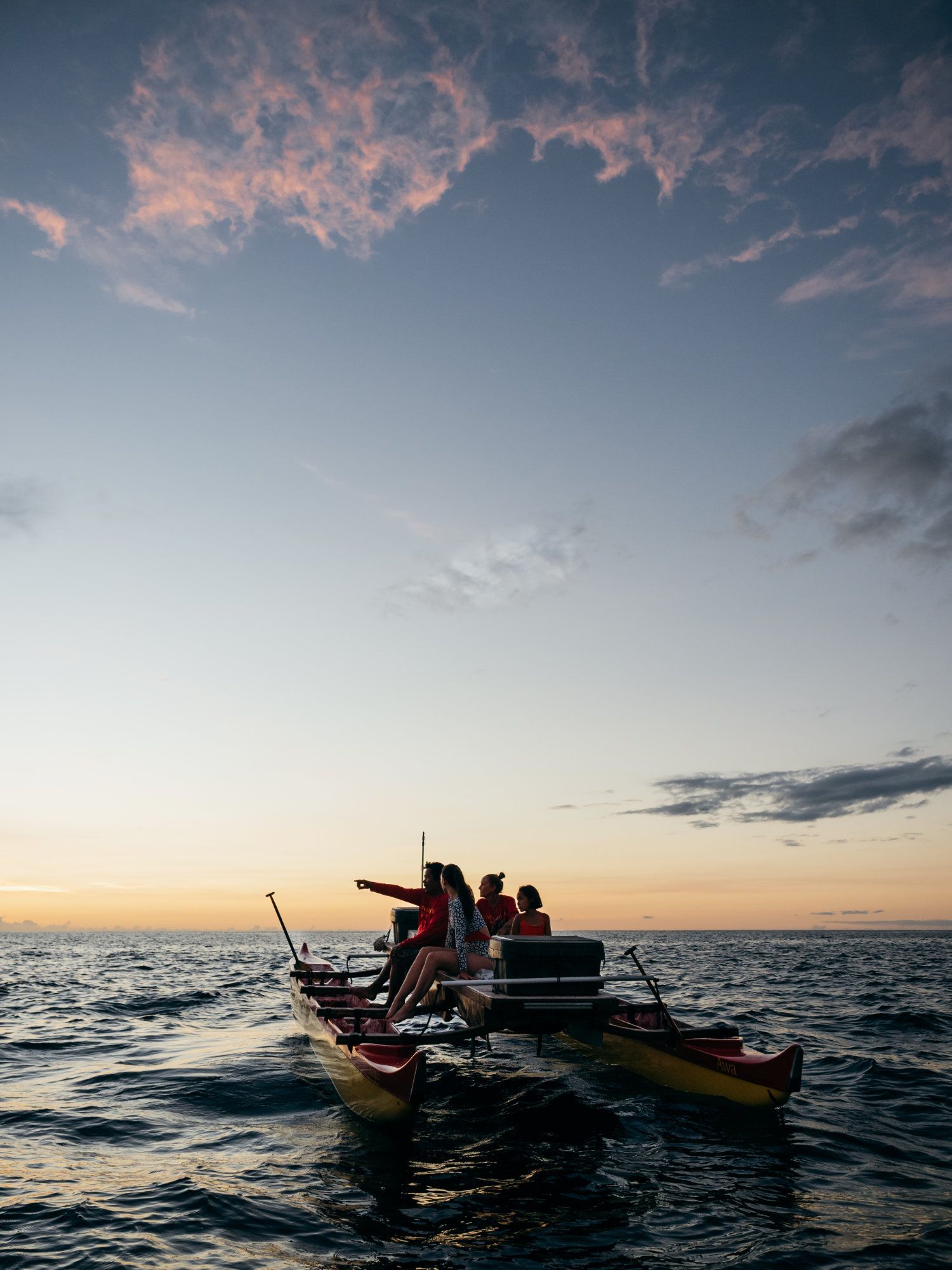 People on a catamaran at sunset, pointing towards the horizon over the ocean.