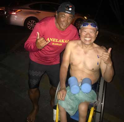 A shirtless man is standing next to a shirtless man in a wheelchair.
