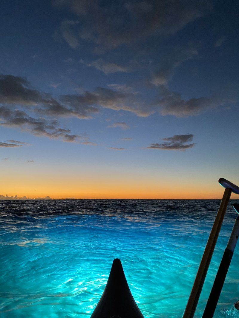 Boat on turquoise water at sunset with orange horizon and cloudy blue sky.