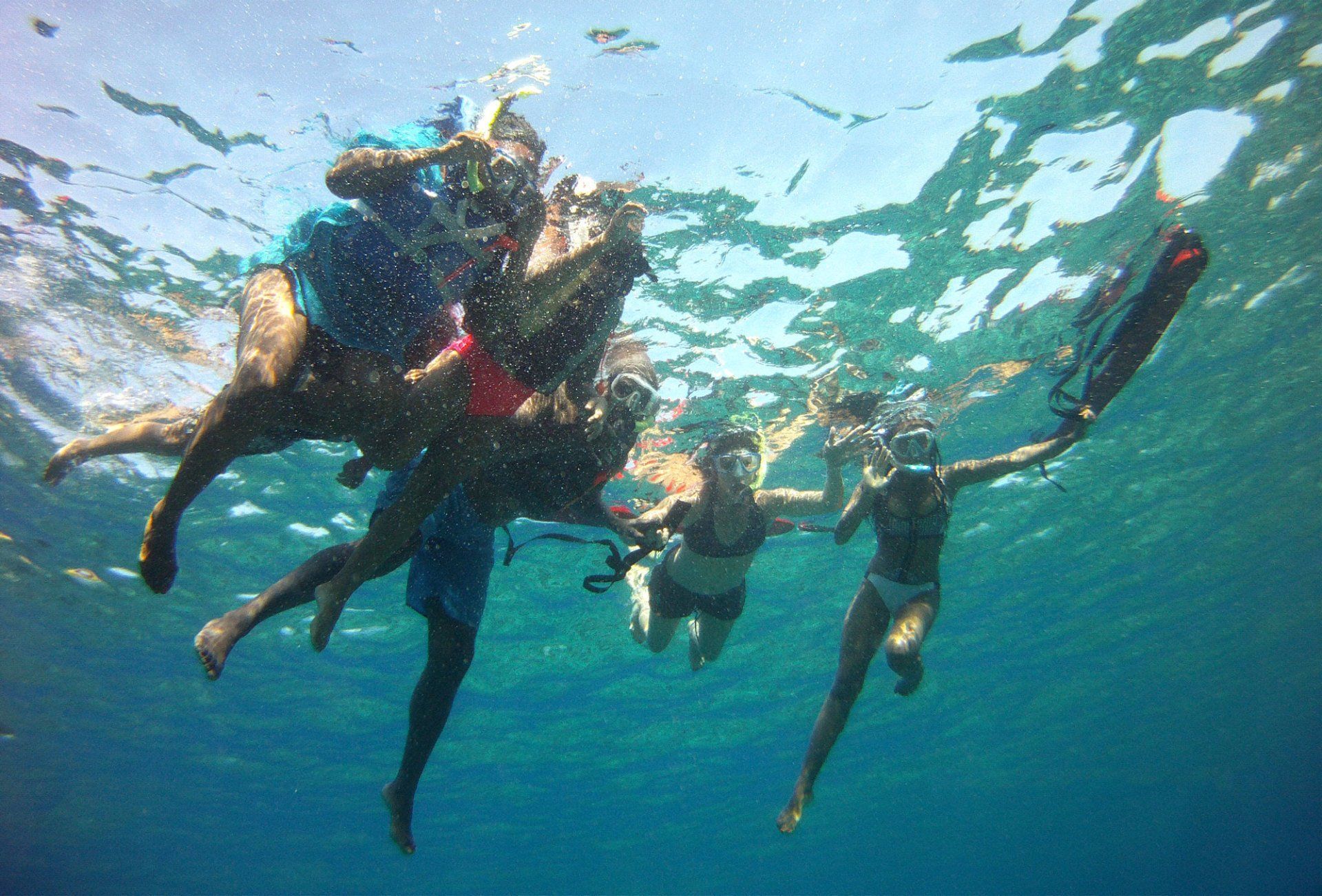 People snorkeling in clear blue water, one holding a black fin, others smiling.