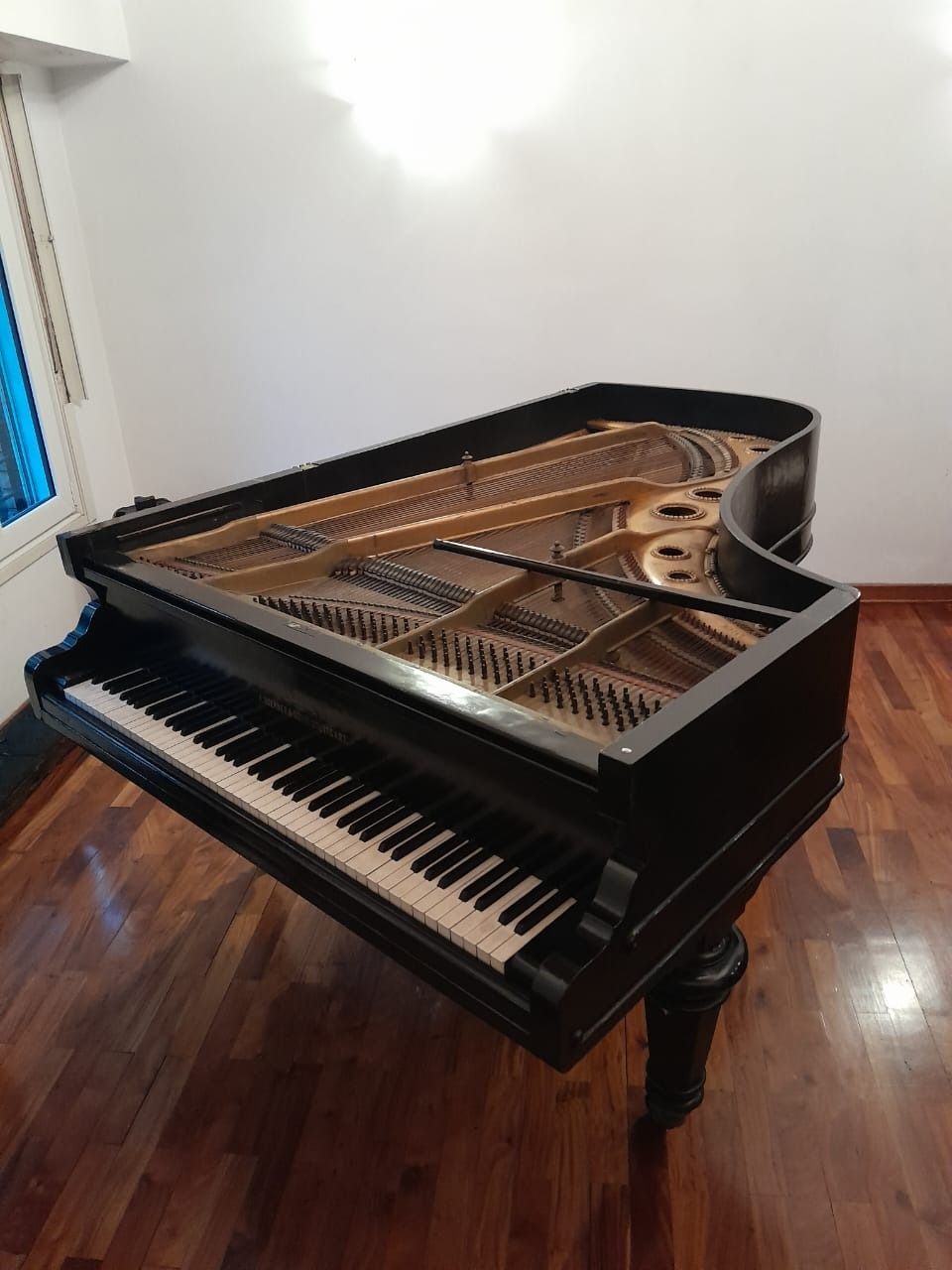 Piano de cola negro en una habitación con pisos de madera, iluminado con luz natural.