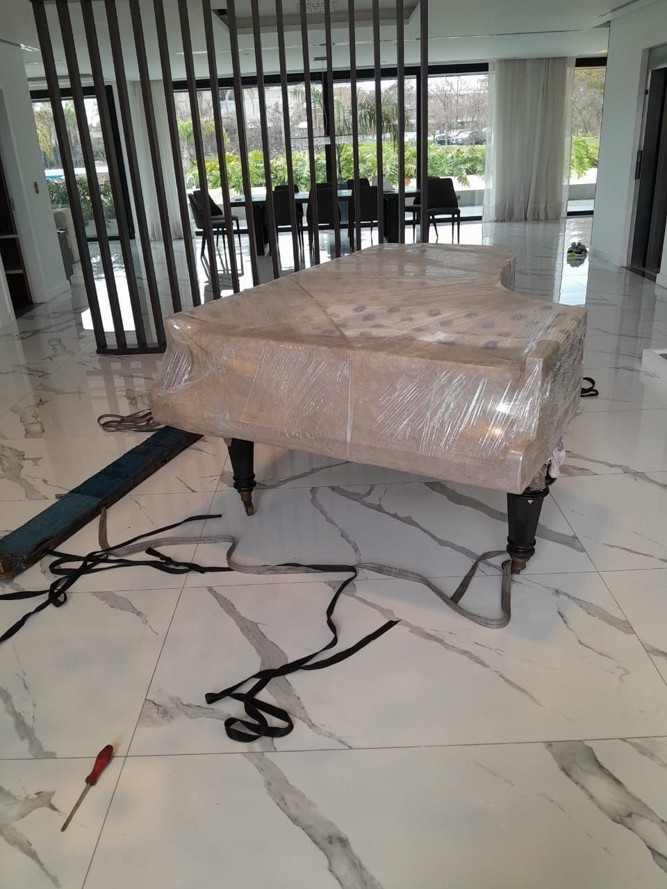 Un piano envuelto en plástico reposa sobre un suelo de mármol. Correas y herramienta.