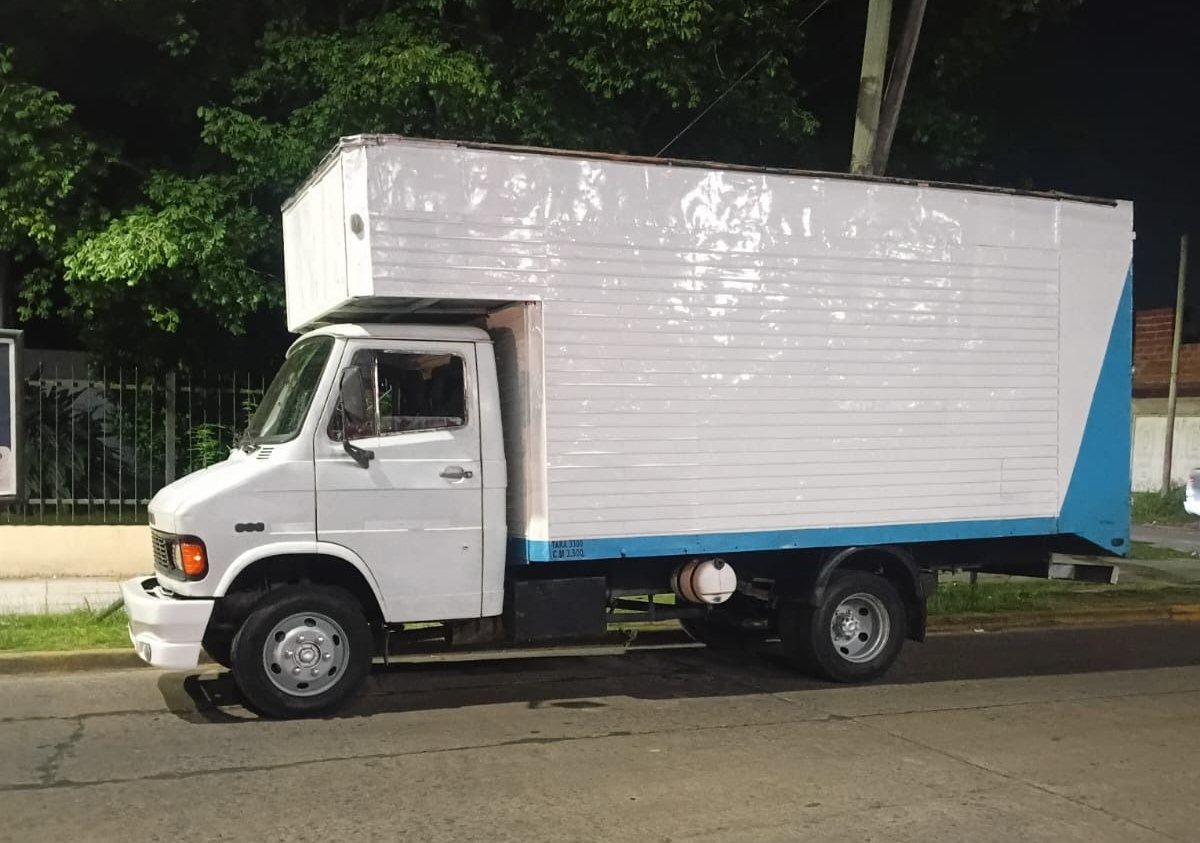 Camión de reparto blanco estacionado en una calle por la noche, con detalles azules en la caja de carga.