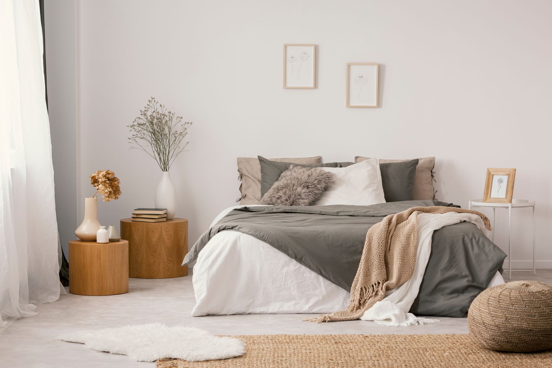 Cozy neutral bedroom with white bed, gray bedding, wood accents, and dried flowers beside the bed