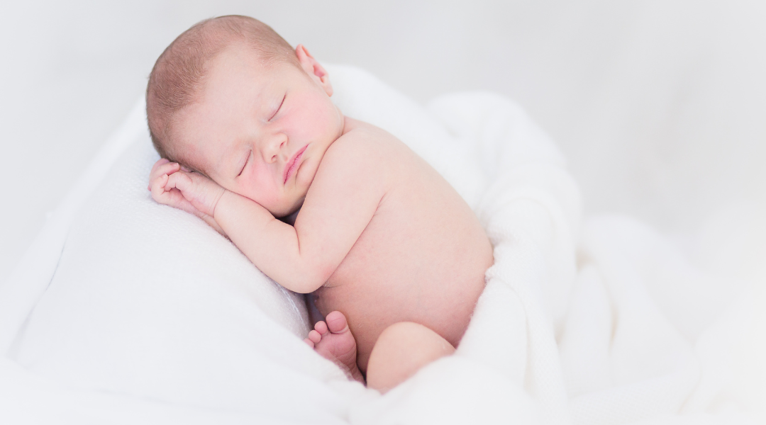 A newborn baby is sleeping on a white blanket.