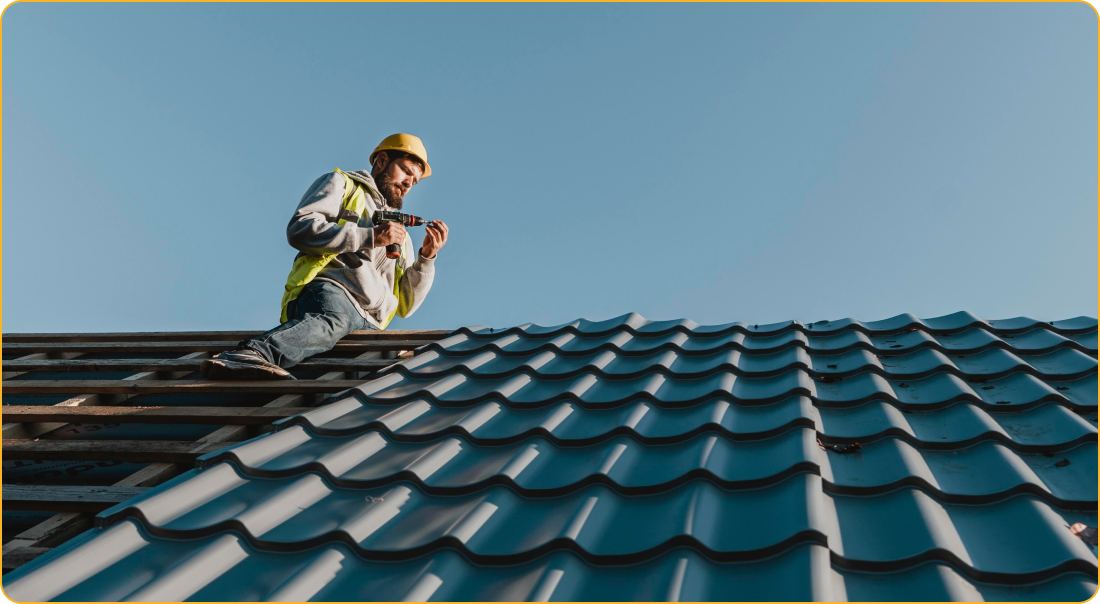 A man is sitting on top of a roof working on it.