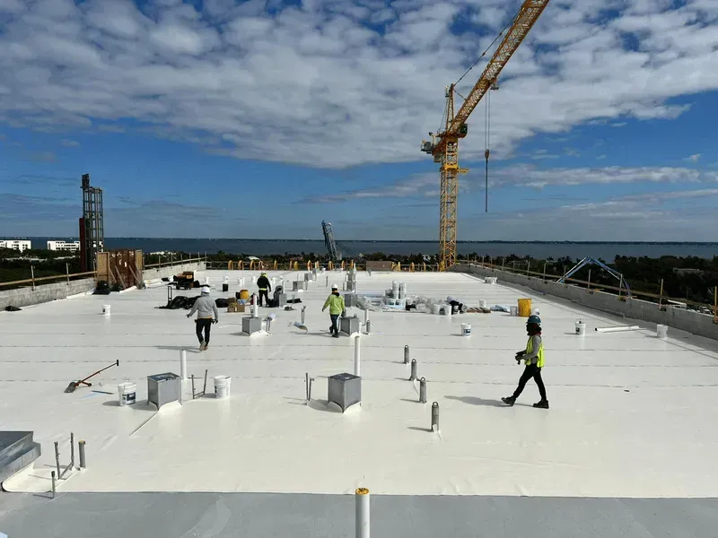 A group of construction workers are working on a white roof.