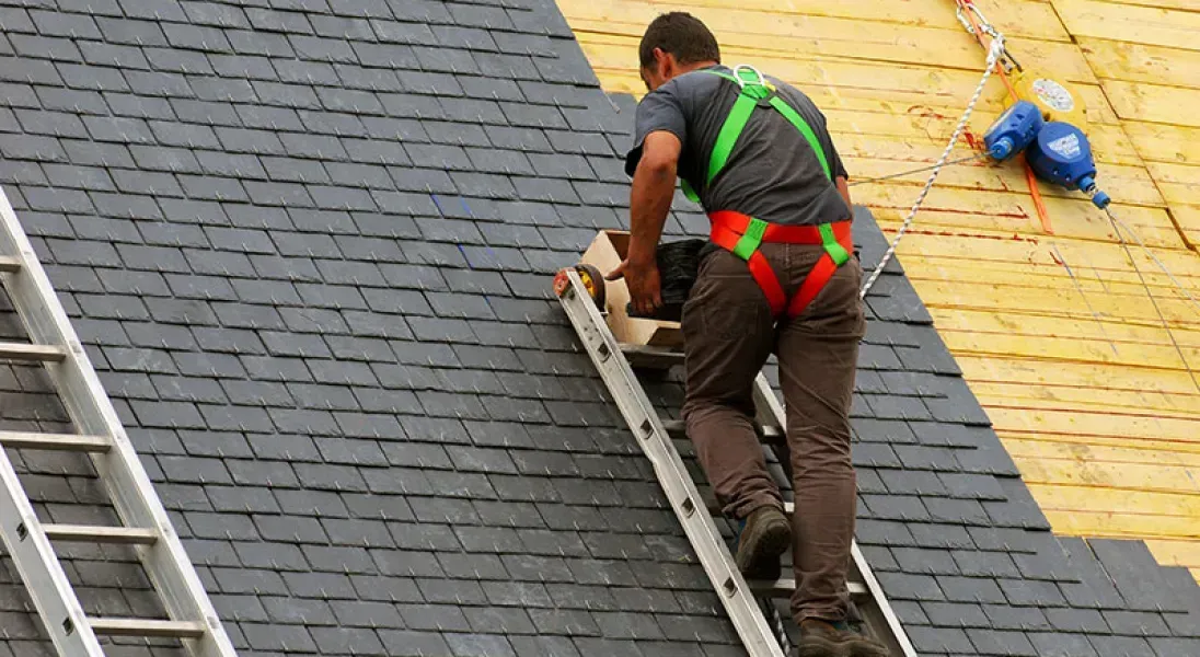 A man is standing on a ladder on top of a roof.