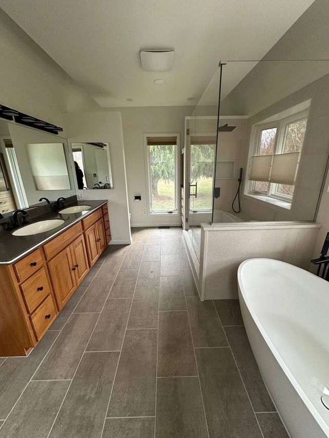 Double vanity with dark granite top, glass shower and freestanding tub, a Handyman on Demand bathroom remodel