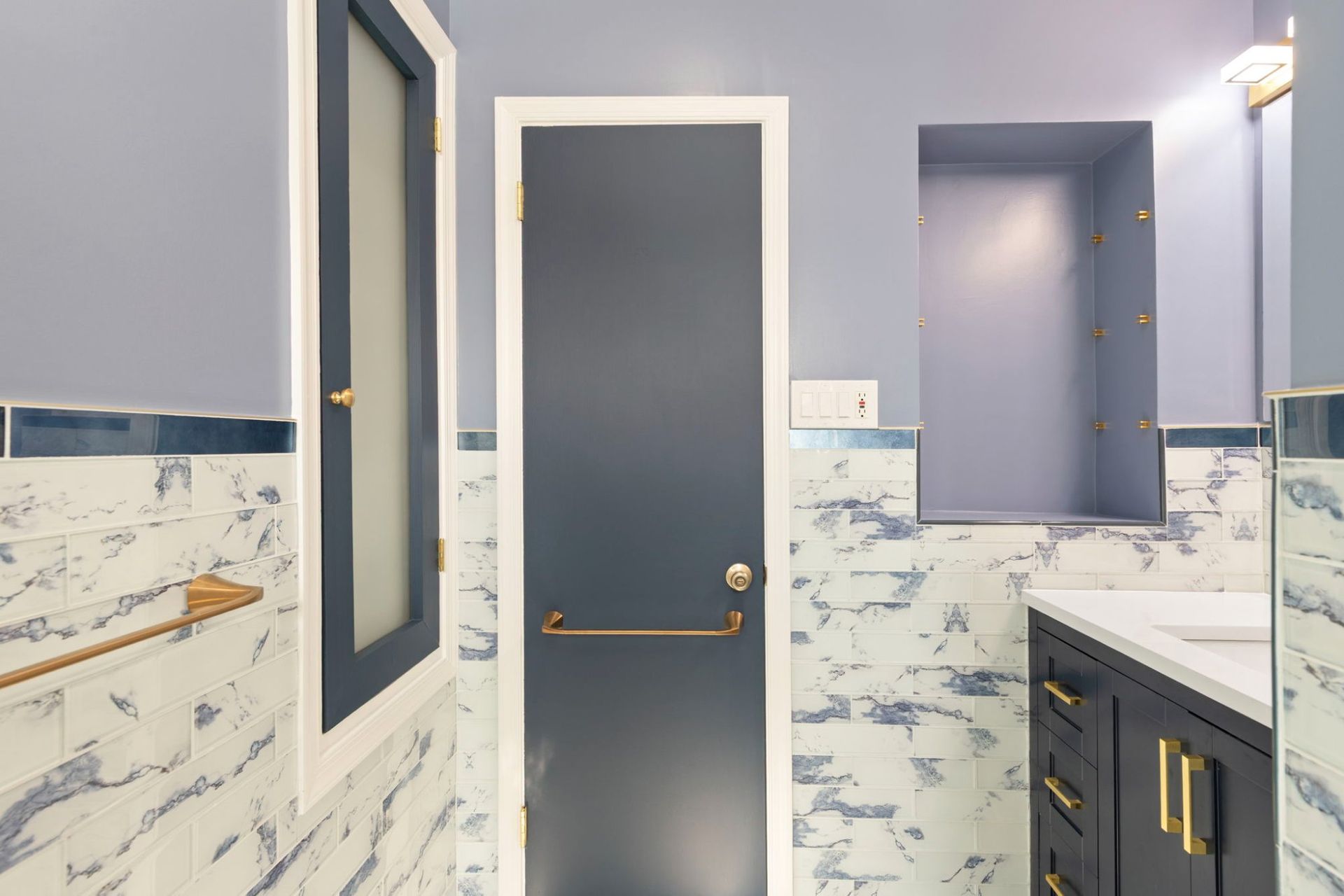 Bathroom remodel with navy accent door, built-in shower niche, and marble tile surround by professional contractor Handyman on Demand serving Ellicott City MD
