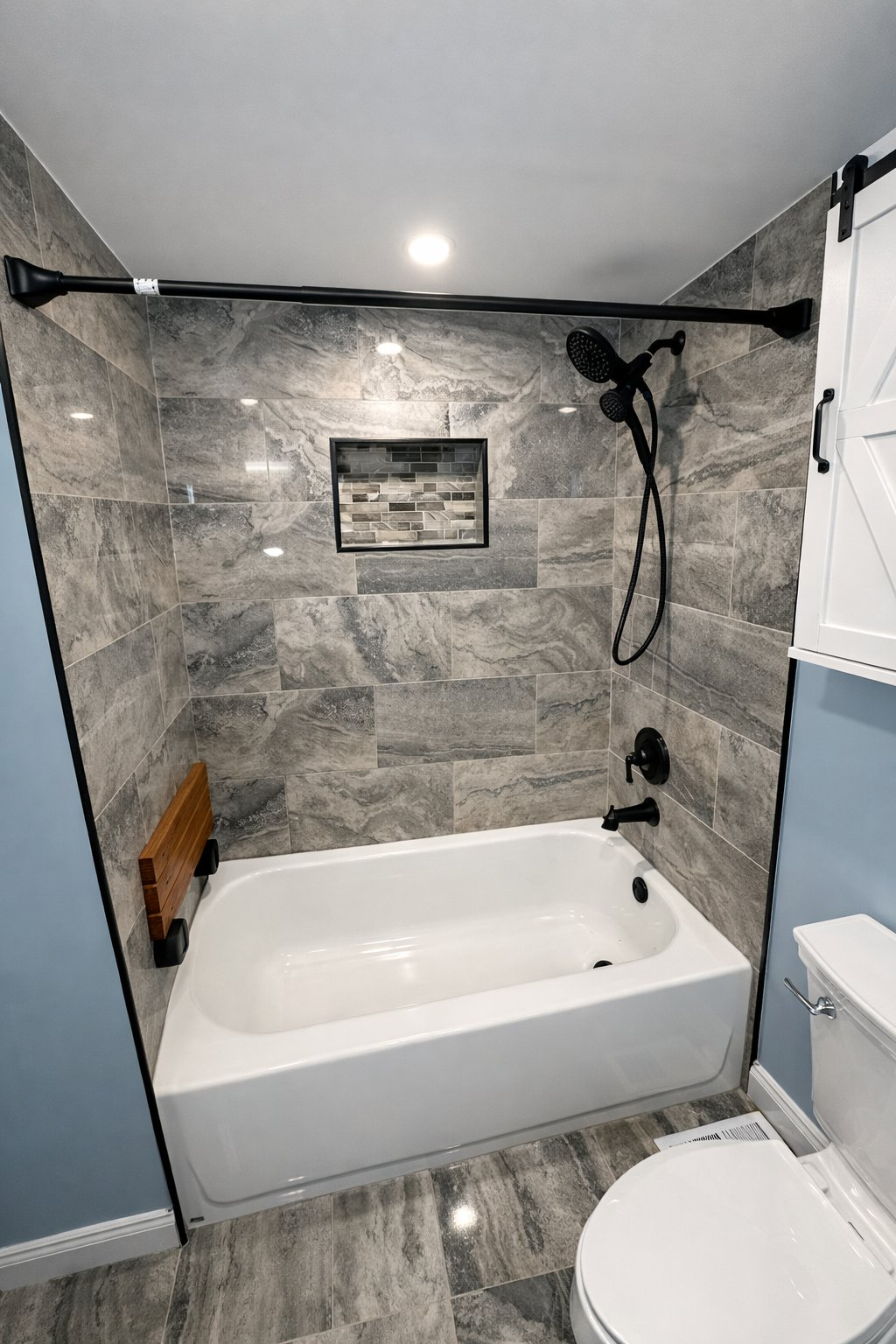 Local bathroom remodel in Baltimore County MD with tub and shower surround, gray stone tile, matte black fixtures, barn door wall cabinet, and recessed niche by Handyman on Demand