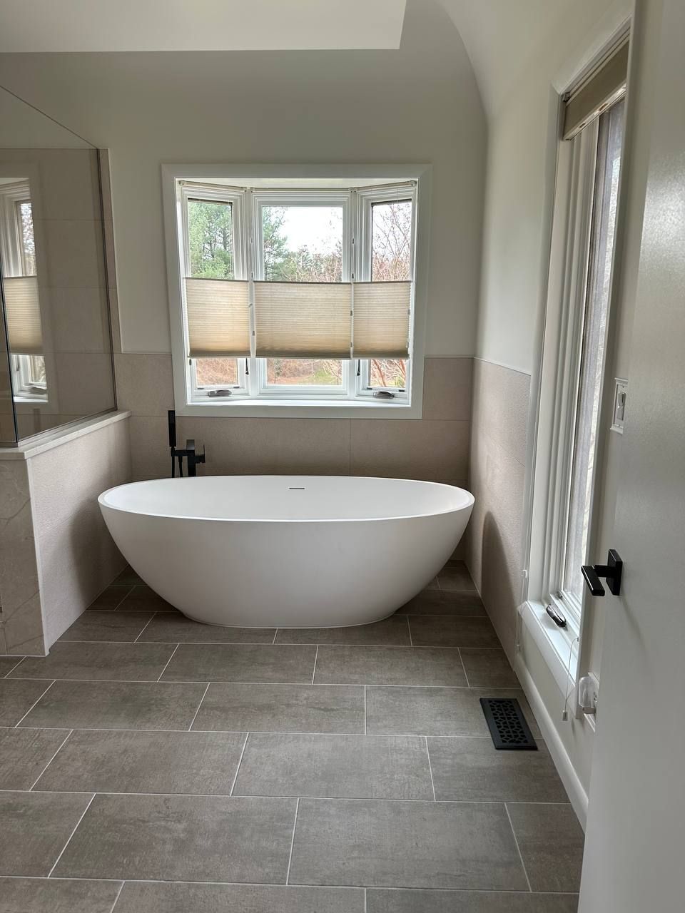 Professional bathroom remodeling and renovation in Baltimore County MD with freestanding soaking tub, large format gray floor tile, and neutral wall tile by Handyman on Demand