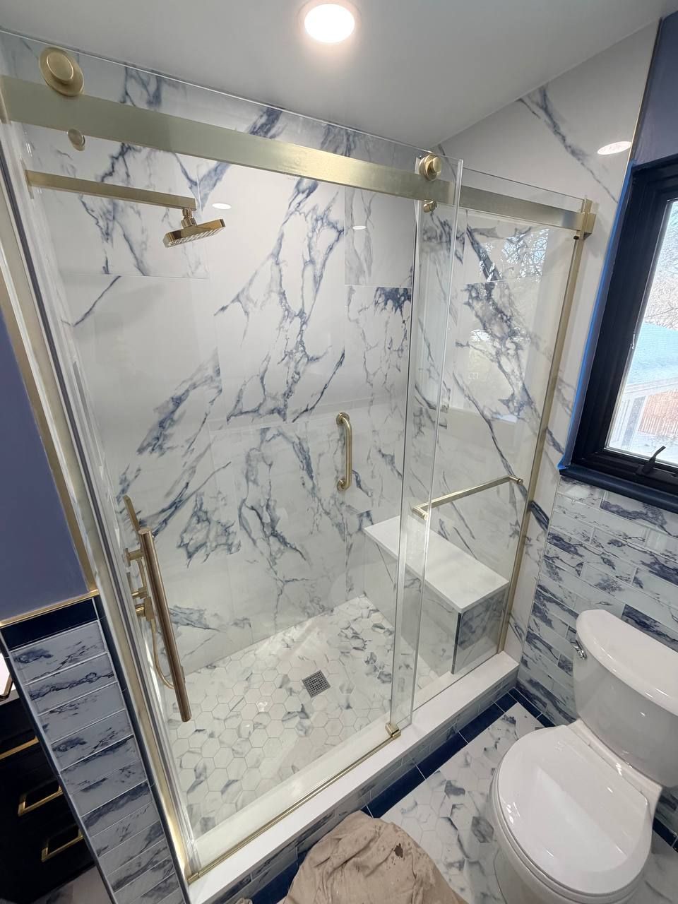 Custom bathroom renovation in Baltimore County MD with blue marble tile walk-in shower, brushed gold sliding glass door, hex floor tile, and navy blue vanity by Handyman on Demand