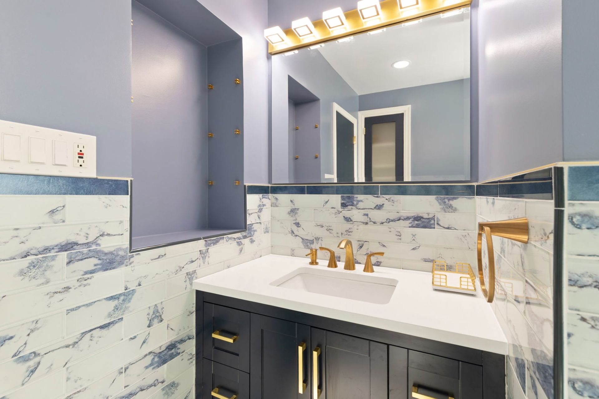 Bathroom renovation featuring new vanity, gold light bar, built-in wall niche, and marble tile by licensed remodeling contractor Handyman on Demand serving Ellicott City MD