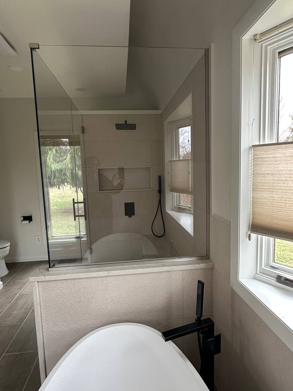 Custom bathroom remodel in Baltimore County Maryland with frameless glass shower enclosure, rainfall shower head, freestanding soaking tub, and matte black fixtures by Handyman on Demand