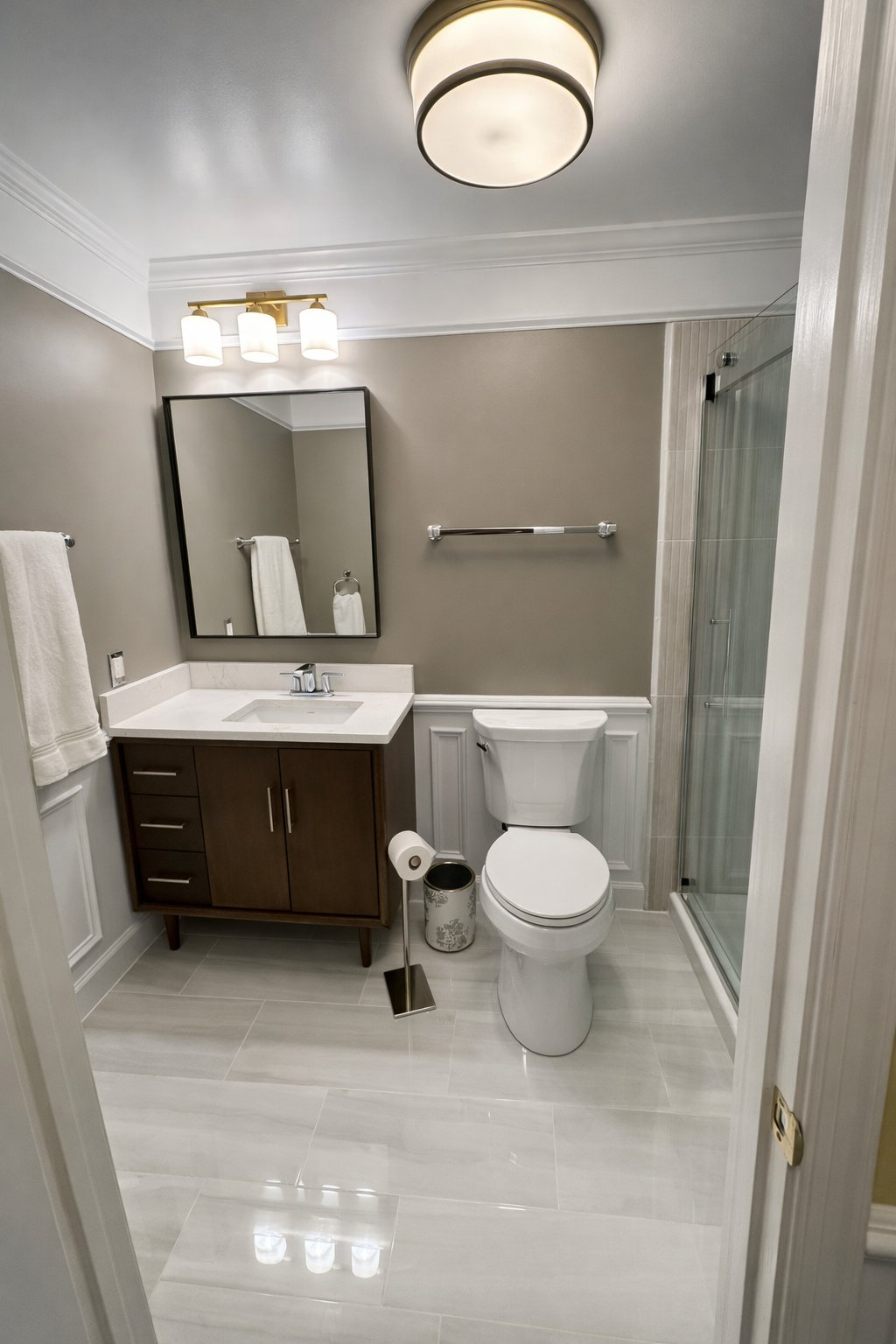 Full bathroom renovation and remodel in Baltimore County MD with dark walnut vanity, white wainscoting, glass shower enclosure, crown molding, and polished large format tile floor by Handyman on Demand