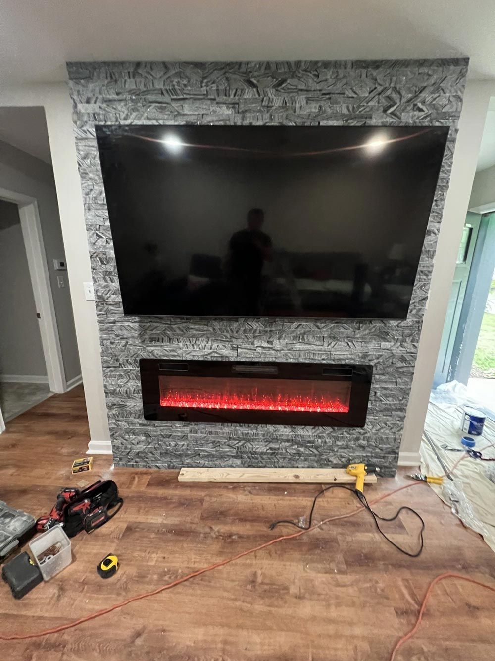 Large-screen TV and electric fireplace installed in a gray stone-clad wall