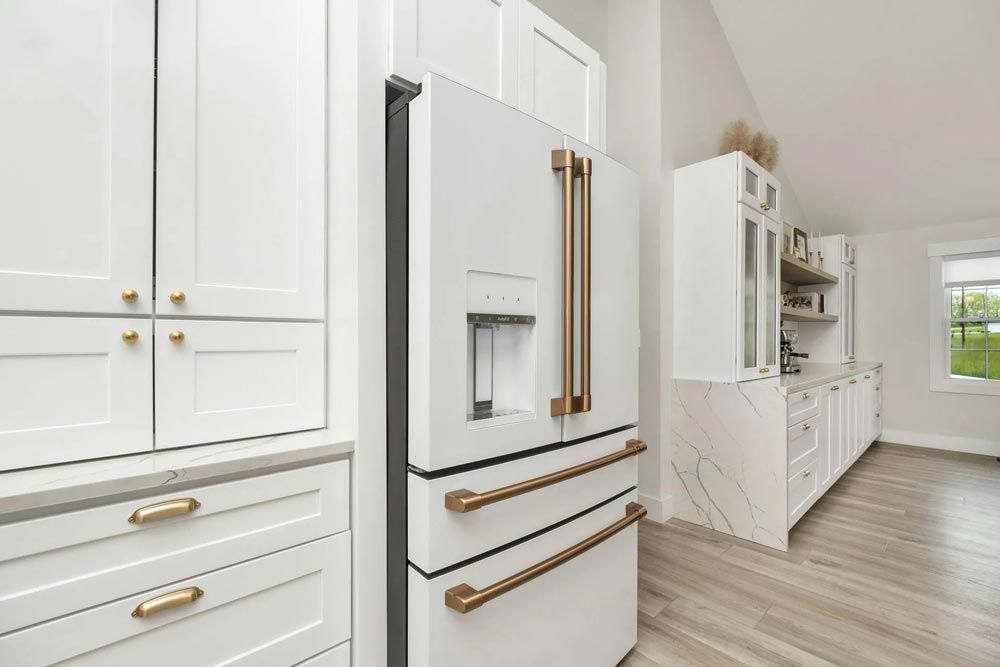 A modern white kitchen with a white refrigerator featuring gold handles