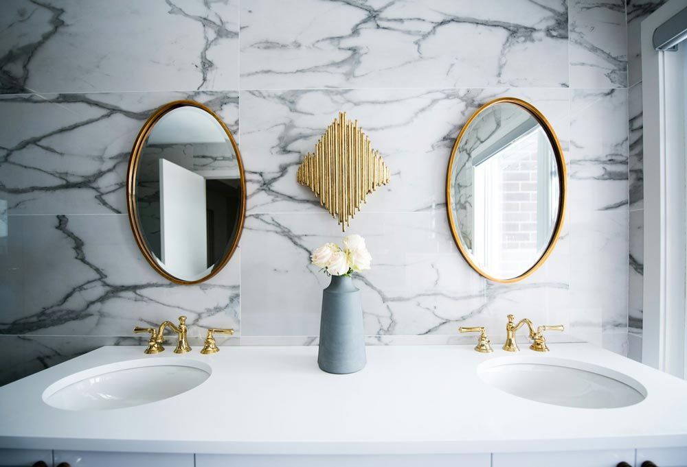 Bathroom with marble wall, dual sinks, gold-framed oval mirrors