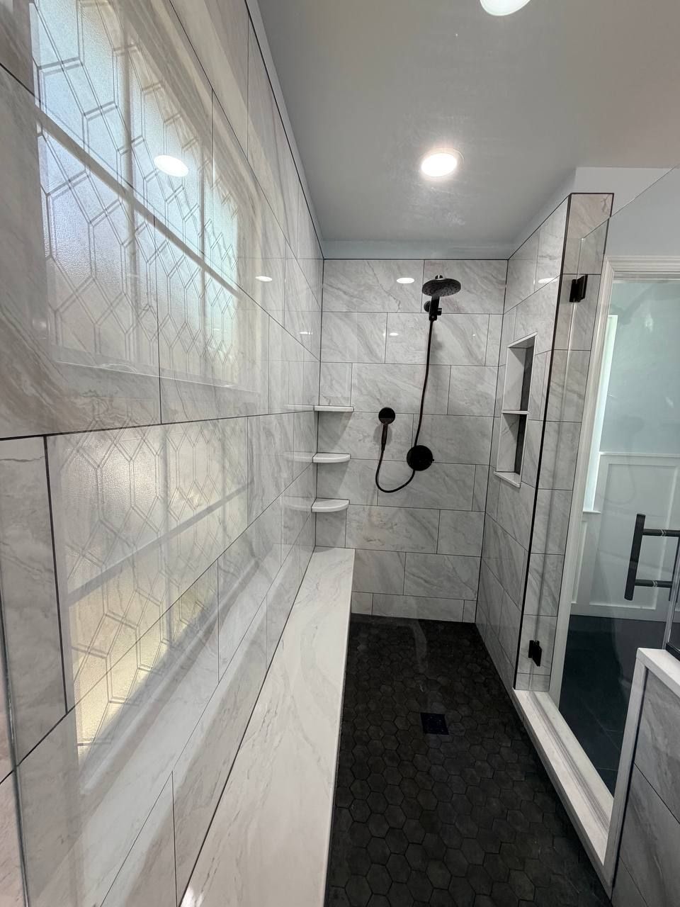 Luxury bathroom remodeling and renovation in Baltimore County MD — walk-in shower with marble tile walls, built-in bench, recessed niche, and black hex floor tile by Handyman on Demand