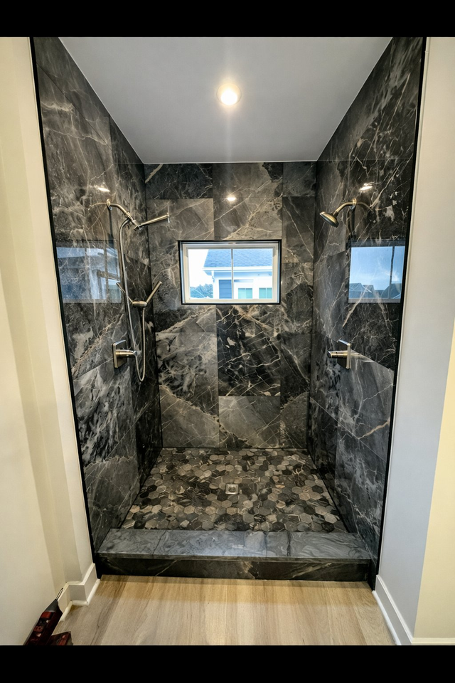 Double shower in dark marble-look tile with pebble floor, a Handyman on Demand bathroom remodel