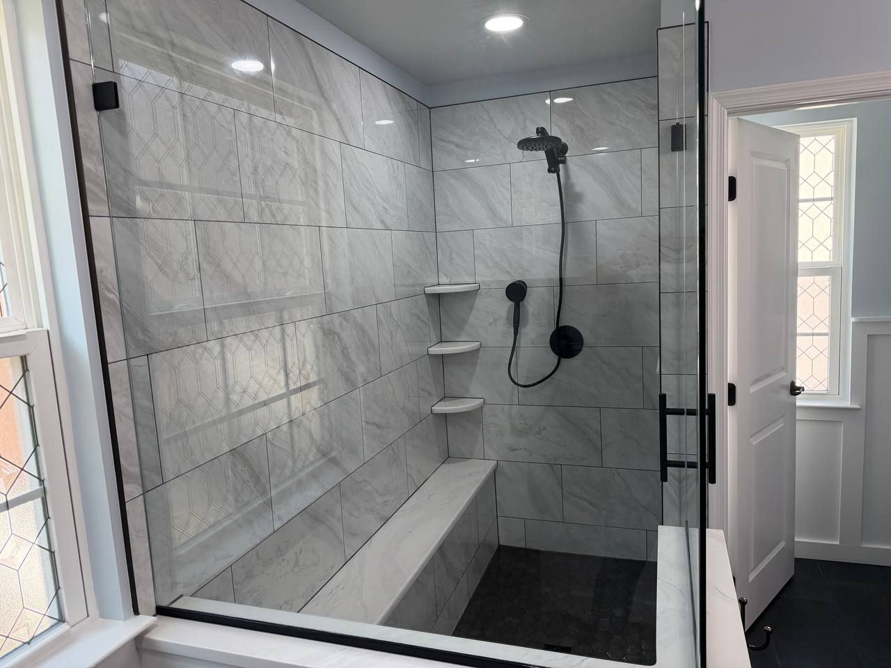 Custom shower remodel and bathroom renovation in Baltimore County MD with white marble tile, built-in bench, triple corner shelves, and matte black fixtures by Handyman on Demand