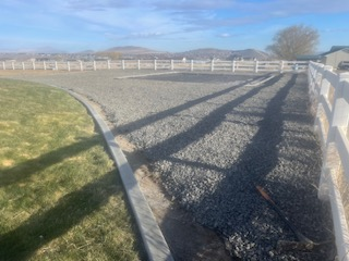 A gravel driveway bordered by a concrete curb and white fence.