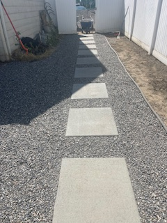 A stone path with square concrete pavers set in gray gravel between two white fences leading to a gate.