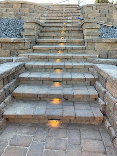 Outdoor stone staircase with built-in, warm-toned step lights illuminating the center of each riser.