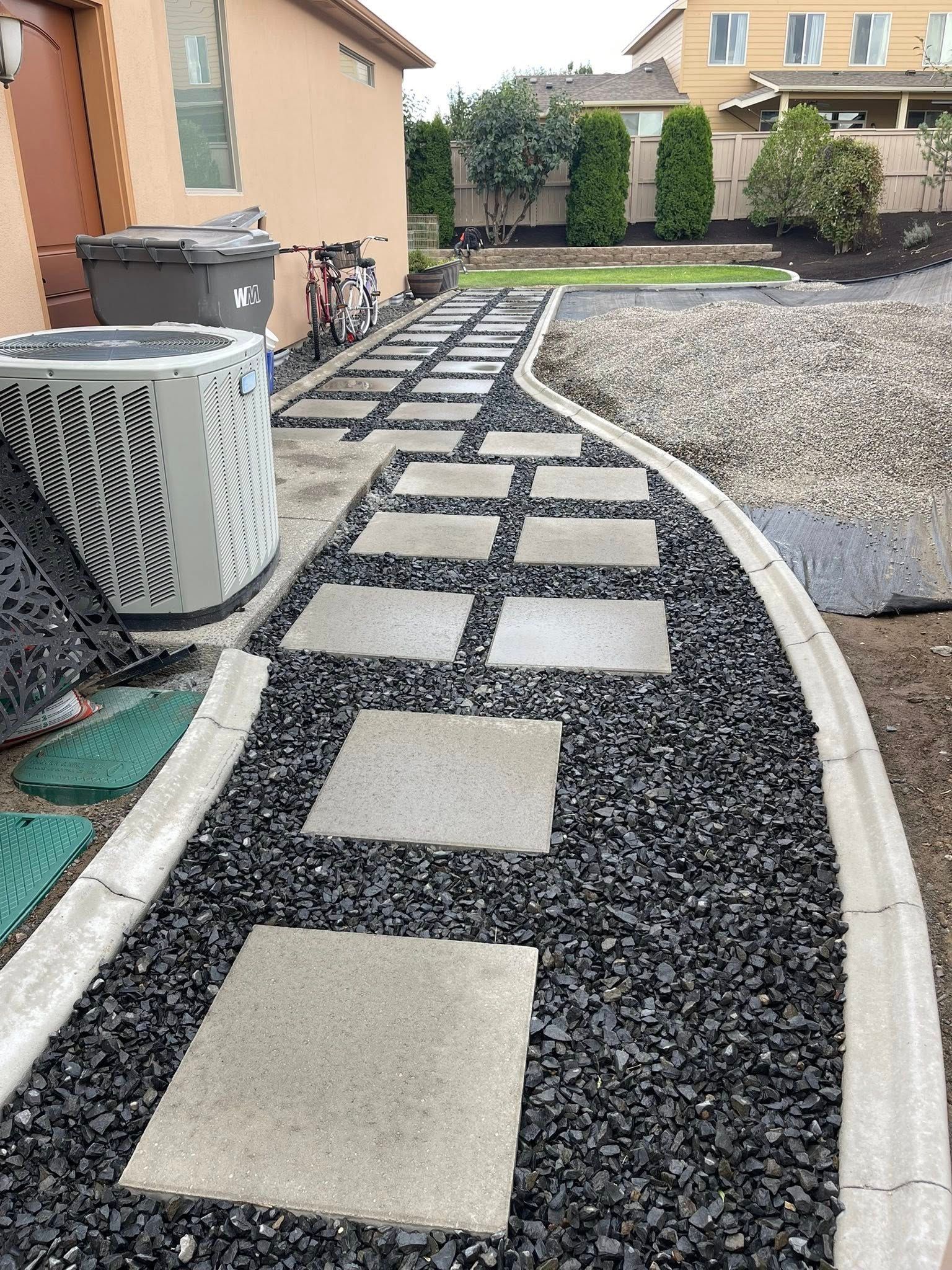 A walkway with square concrete pavers set in black gravel.