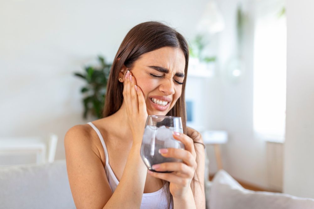 Frau hat Zahnschmerzen beim Trinken von eiskaltem Wasser.