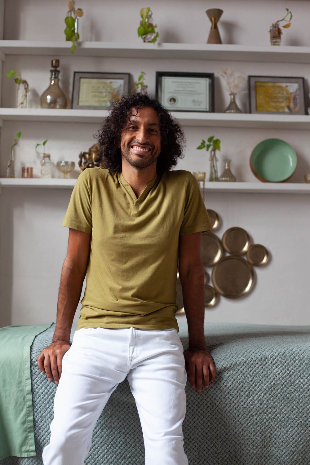 A man in a green shirt and white pants is leaning on a bed.