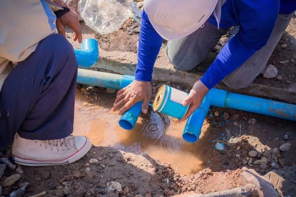 Two Plumbers Repair a Broken Blue Pipe in a Muddy Outdoor Setting — Ballarat Blockages & Plumbing in Wendouree, VIC