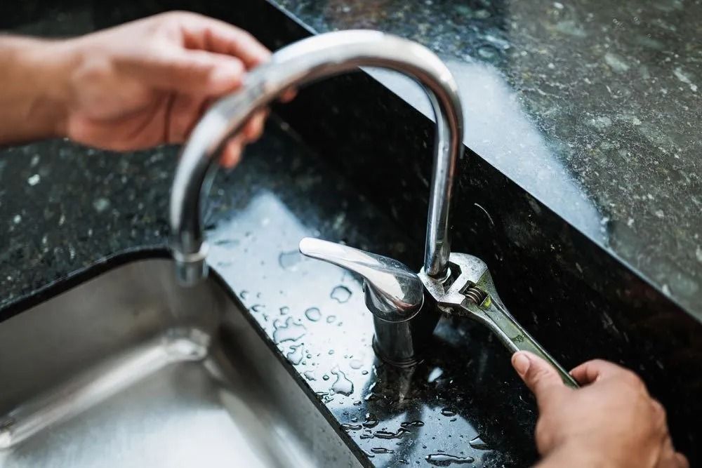 Person Using Wrench to Repair a Silver Kitchen Faucet Next to a Sink — Ballarat Blockages & Plumbing in Wendouree, VIC