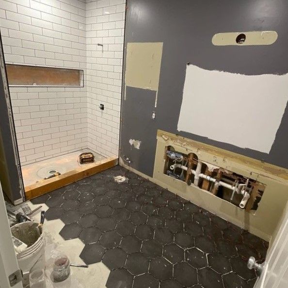 A bathroom under construction with white brick walls and a black tile floor.