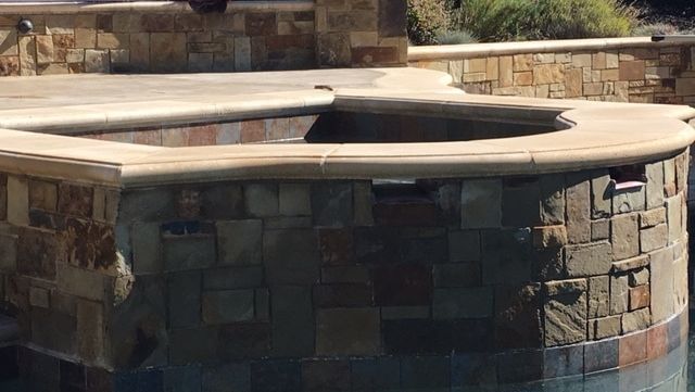 A hot tub in the middle of a swimming pool surrounded by stone walls.