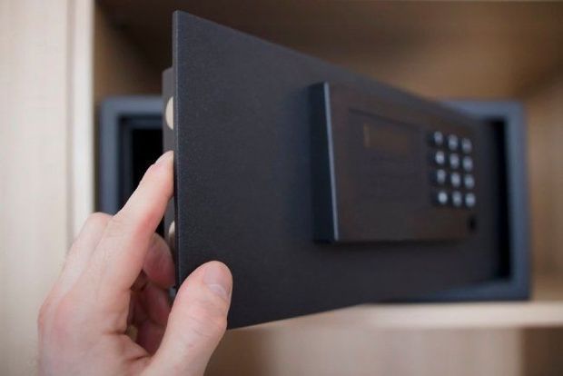 Apertura manuale di una porta di cassaforte nera con serratura a tastiera all'interno di un armadio di legno.