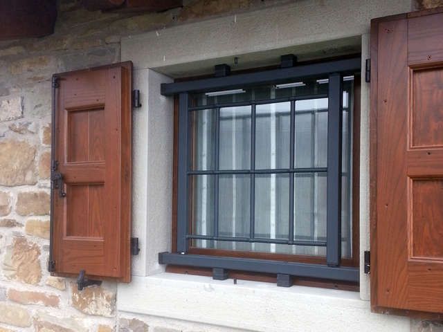 Muro in pietra con finestra a sbarre e persiane in legno marrone su entrambi i lati.