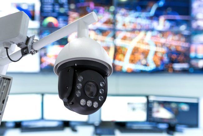 Telecamera di sicurezza in una sala di controllo con monitor di sorveglianza sfocati sullo sfondo.