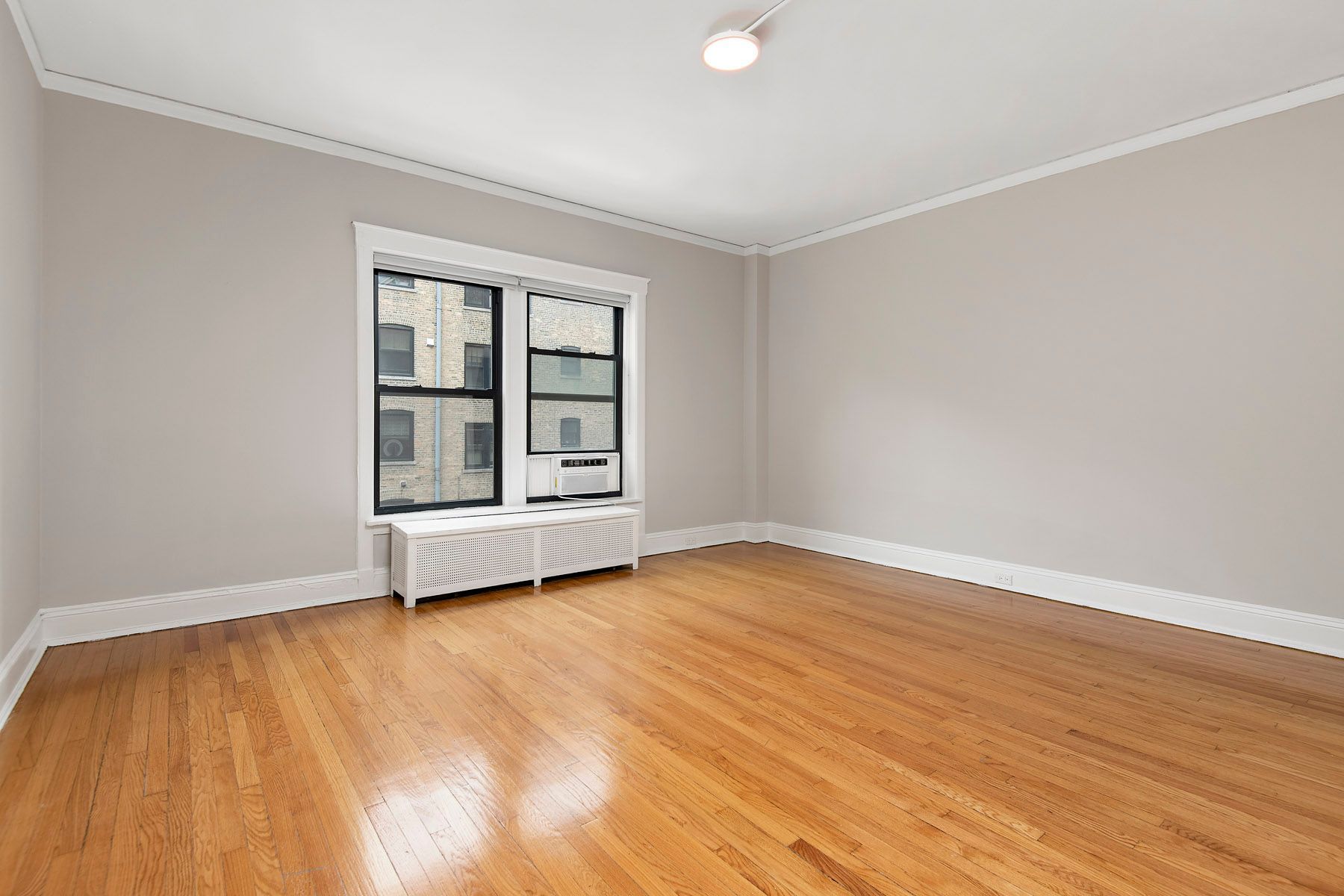 An empty living room with hardwood floors and a window at Park Fullerton by Reside. 