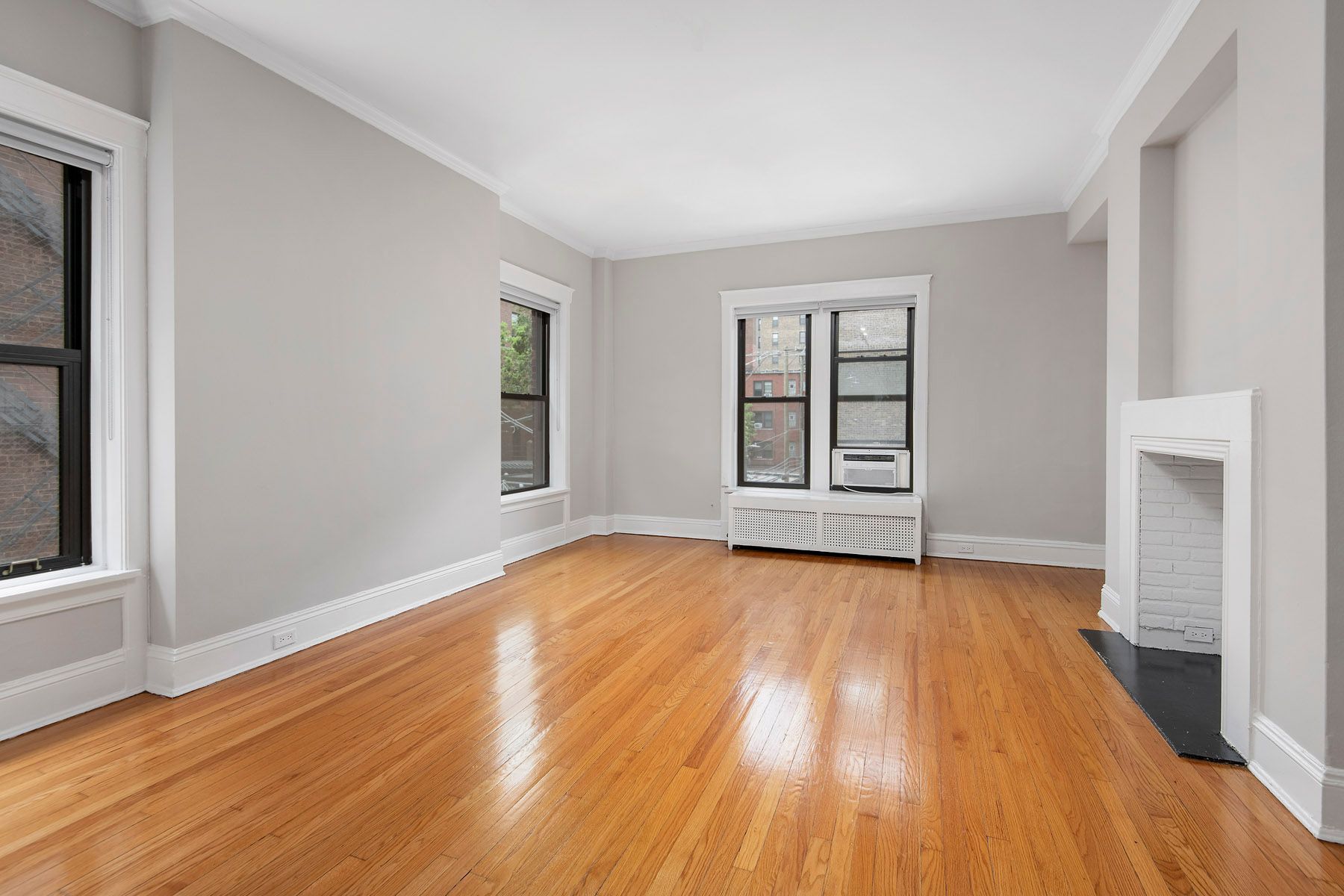 An empty living room with hardwood floors and a fireplace at Park Fullerton by Reside. 