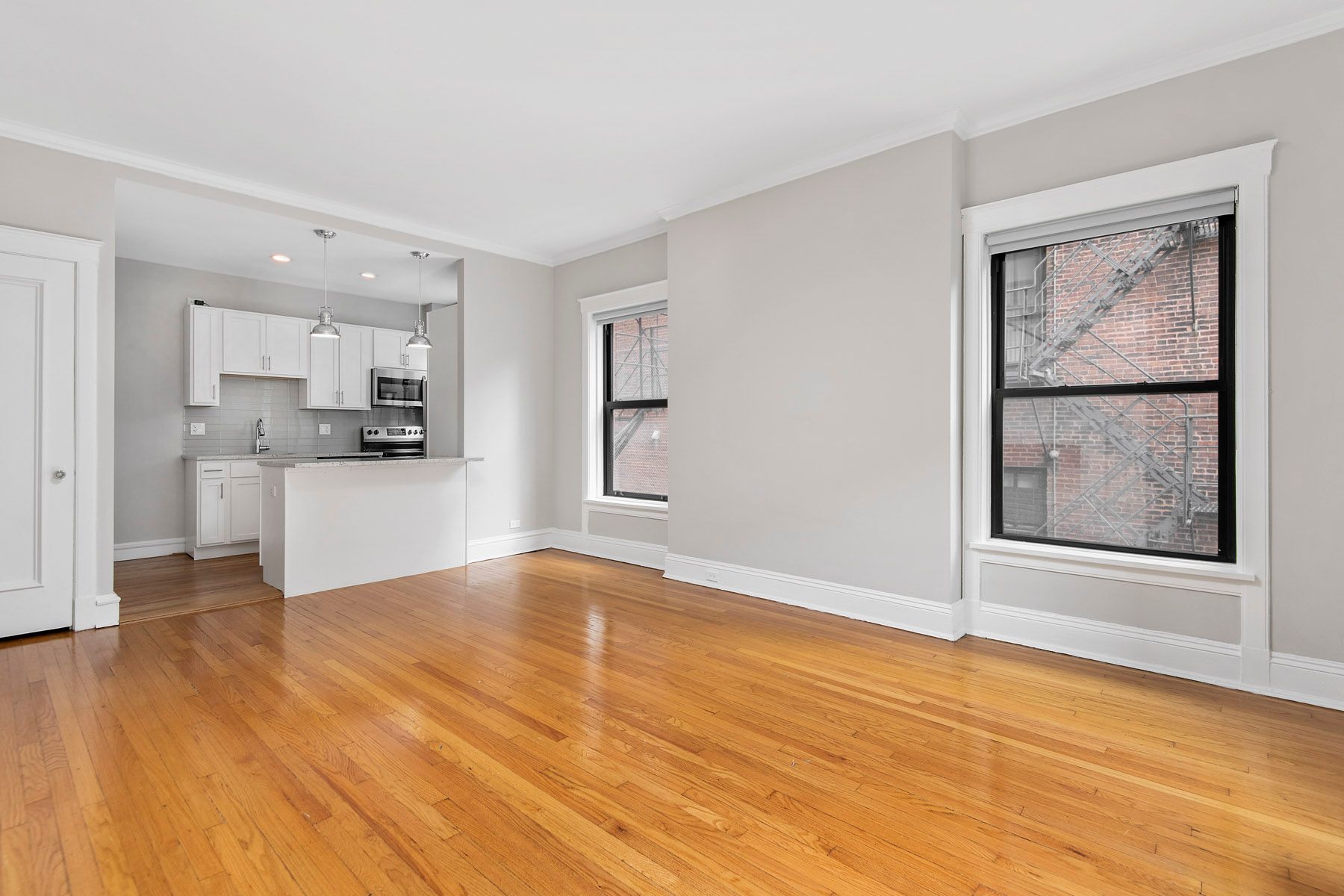 An empty living room with hardwood floors and a kitchen in the background at Park Fullerton by Reside. 