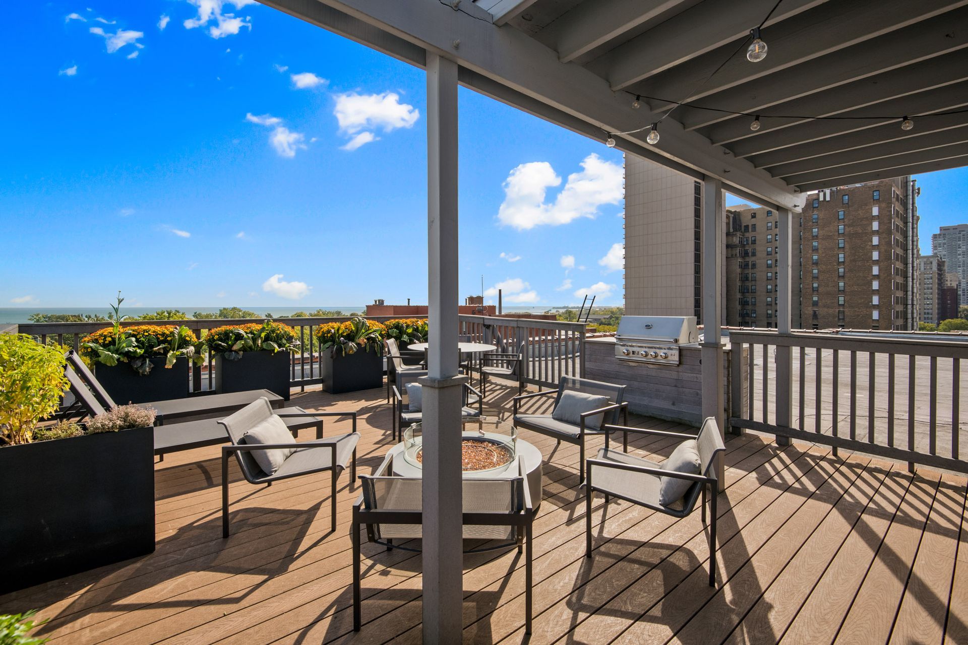 A rooftop deck with a fire pit, chairs, tables, and a grill at Park Fullerton by Reside. 