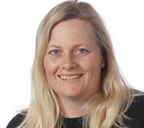 Kvinde med blond hår, der smiler, iført en sort skjorte, mod en hvid baggrund.