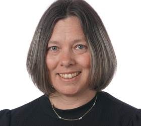 Kvinde med skulderlangt gråt hår smiler, iført en sort skjorte og halskæde.