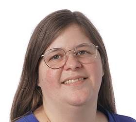 Kvinde med langt brunt hår og briller smiler.