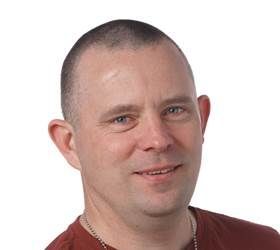 Mand med kort hår og et let smil i en rød skjorte mod en hvid baggrund.