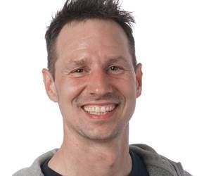 Mand med kort brunt hår smiler til kameraet iført en grå hættetrøje.